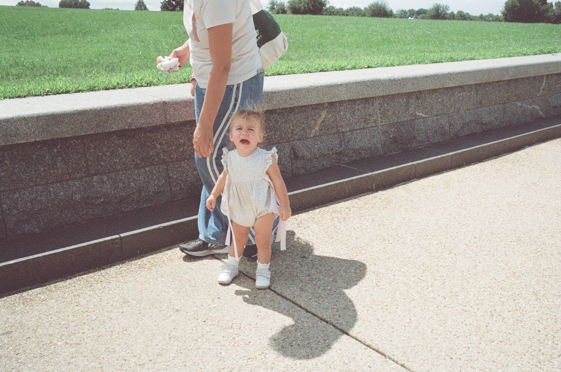 Toddler crying while standing next to an adult in a park