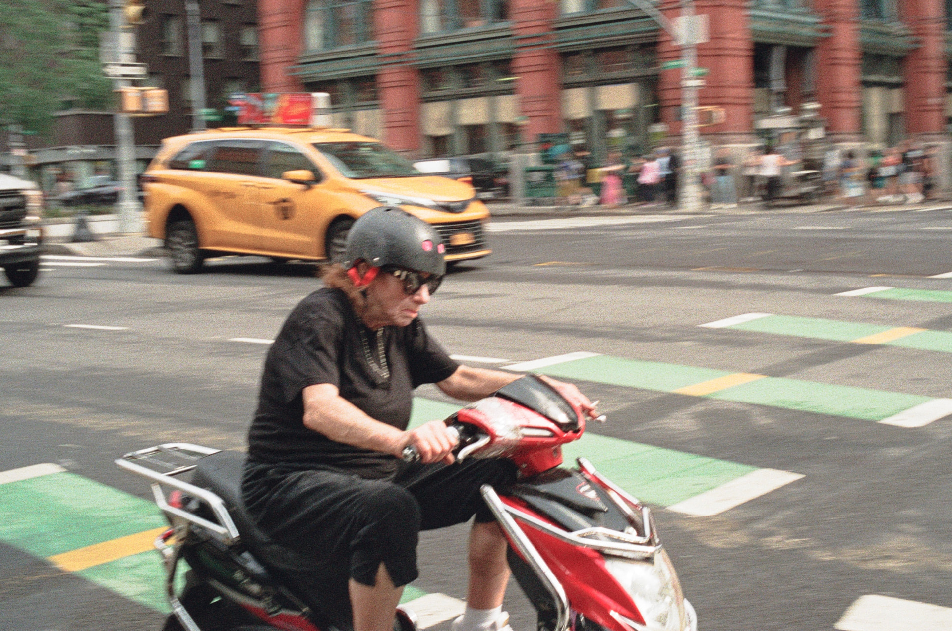 Blurred man in sunglasses riding a red scooter through an intersection