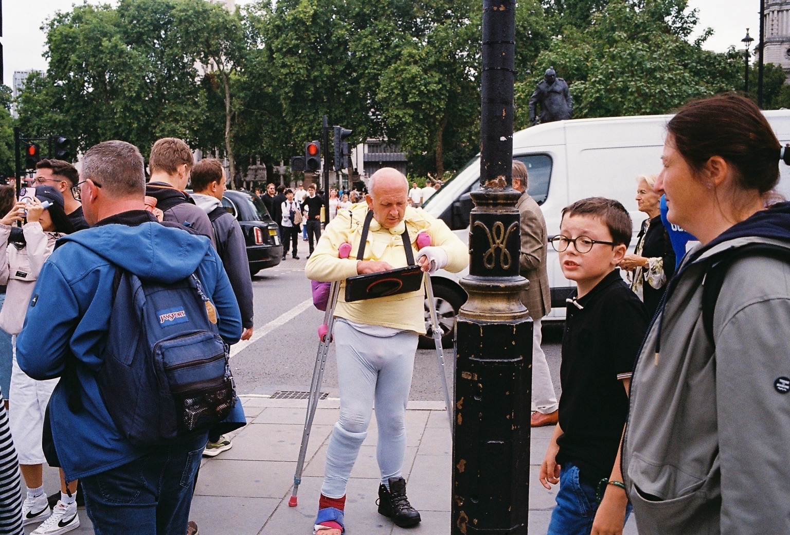 Man on crutches in a yellow sweatshirt checking a tablet in a crowd near Westminster