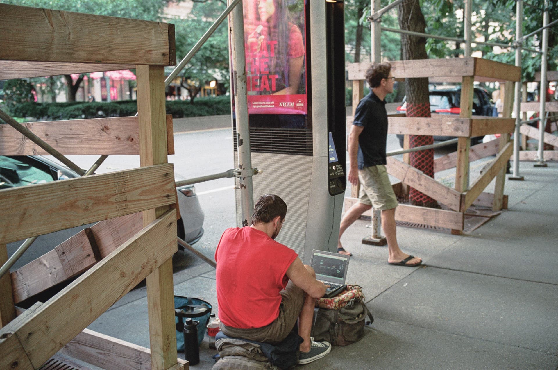 Man in a red shirt working on a laptop on a city sidewalk