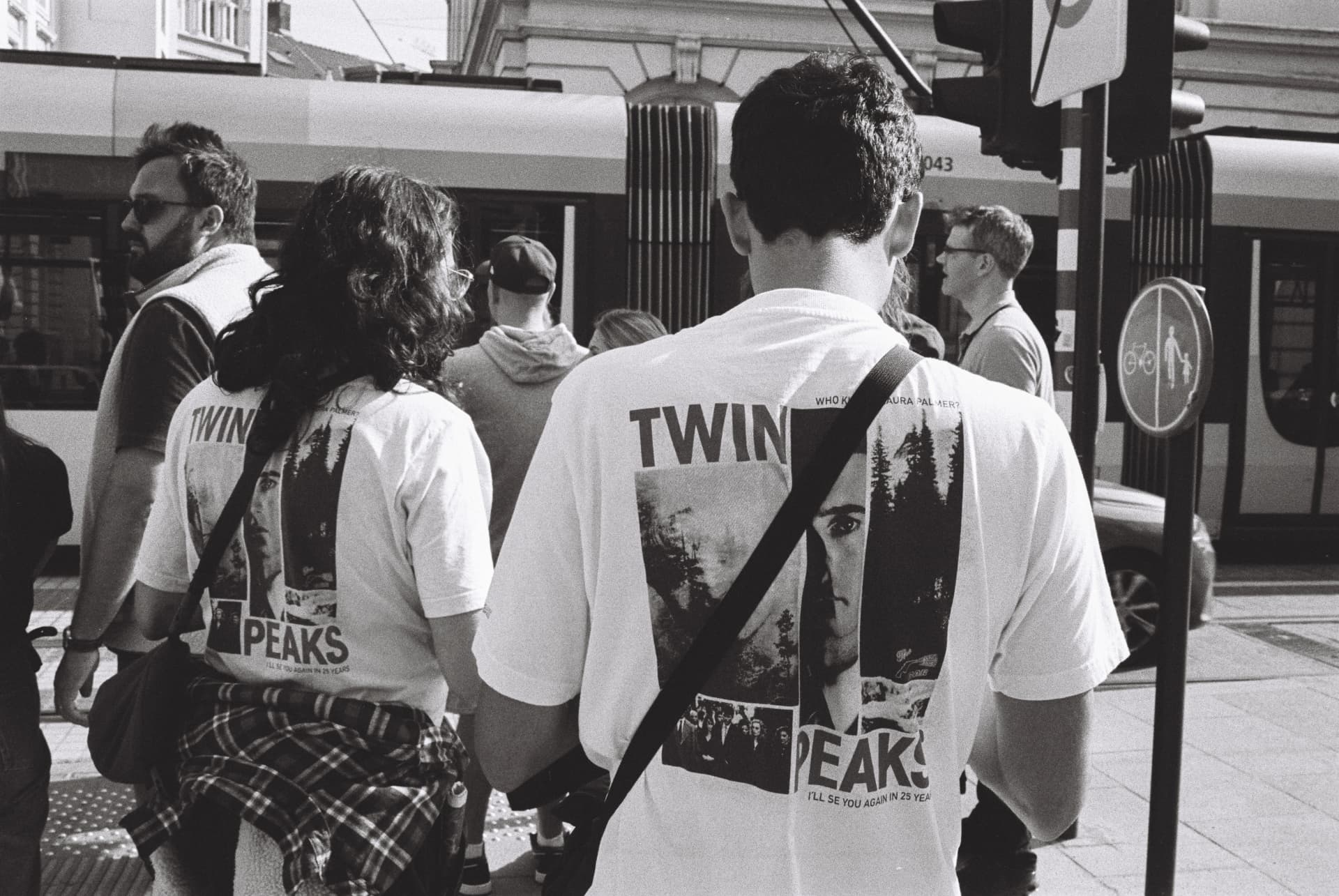 Two people wearing Twin Peaks t-shirts at a tram stop in black and white