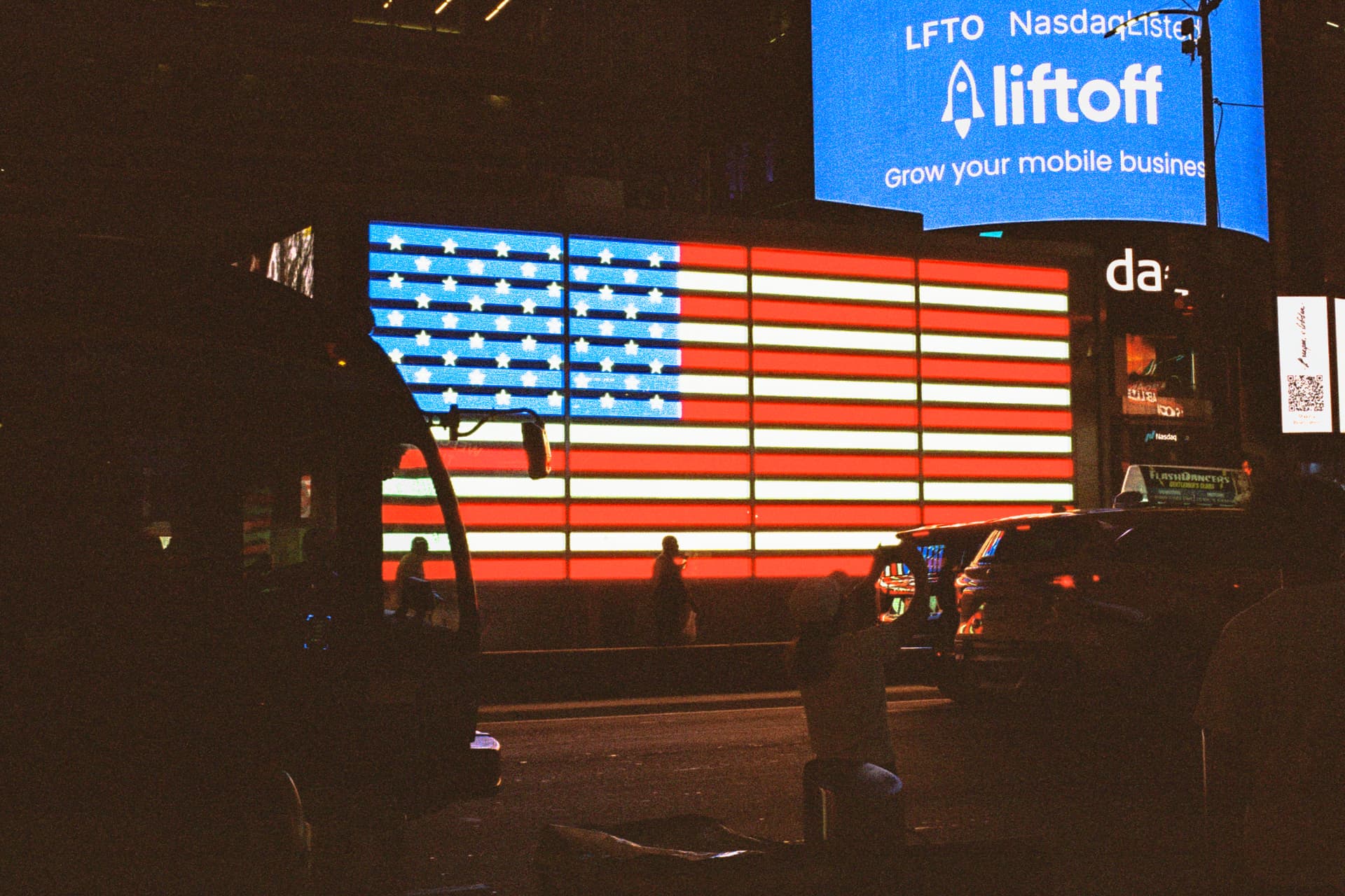 Giant American flag billboard glowing over Times Square traffic at night