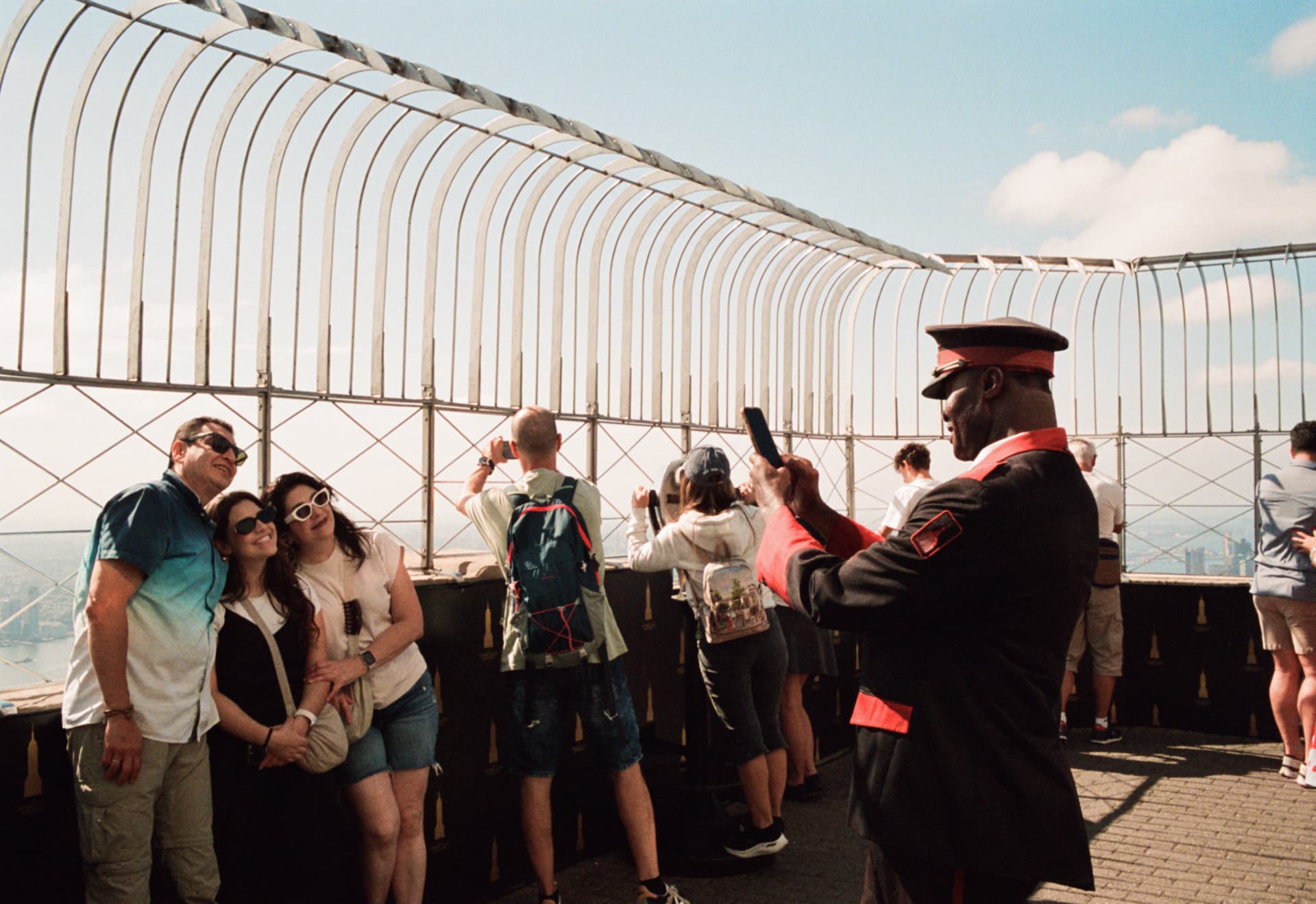 Attendant in a red-trimmed uniform taking a selfie on an observation deck with tourists posing nearby